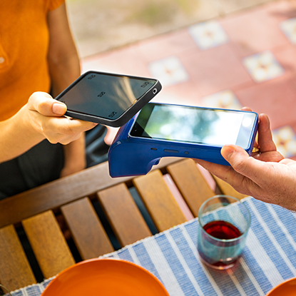 Two people making a contactless payment outdoors, one holding a smartphone near a handheld card reader